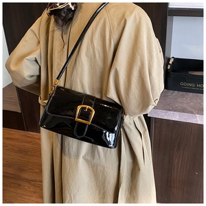 Détail d'un sac baguette en cuir verni noir avec boucle carrée dorée et bandoulière fine