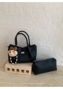 Vue détaillée du sac à main noir en cuir grainé avec fermoir argenté et charm chien