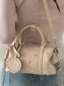 Sac Boston beige chic avec clous étoiles et breloque cœur vu sous un angle latéral