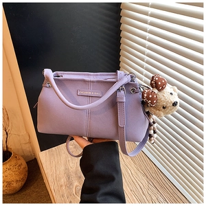 Detail view of purple lavender handbag featuring a cute teddy bear charm and gold emblem