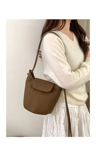 Detail of a brown leather bucket bag with vertical stitching and curved flap closure