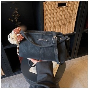 Detail of black textured crossbody bag with fashion label and cute plush bear charm
