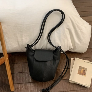 Close-up of black lychee grain leather bucket bag with flap closure on wooden floor