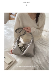 Detail of silver metallic hobo bag with pleated texture and white plush pendant accessory