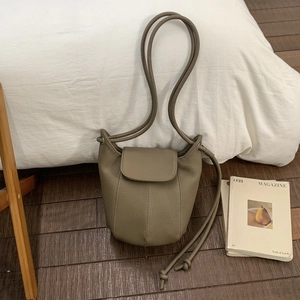 Close-up of khaki pebbled leather bucket bag featuring drawstring knots and flap closure