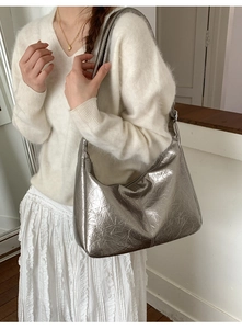 Detail of silver metallic hobo bag with pleated texture worn by model in light studio