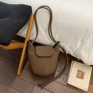Close-up of brown litchi grain leather bucket bag with flap closure on wooden floor