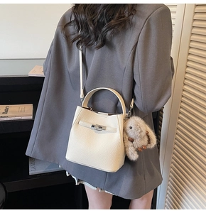 Detailed shot of white lychee leather bucket bag featuring a plush bunny charm and silver buckle