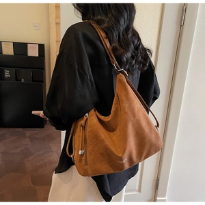 Brown suede tote bag with silver zipper shown on shoulder in a stylish interior setting