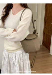 Close-up of earth tone leather bucket bag with white stitching on female model