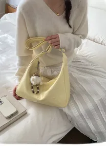 Detail of pale yellow hobo bag with vintage leather texture and cute plush pendant