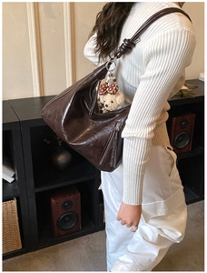 Dettaglio borsa hobo marrone lucido con tracolla annodata e accessorio orsetto peluche
