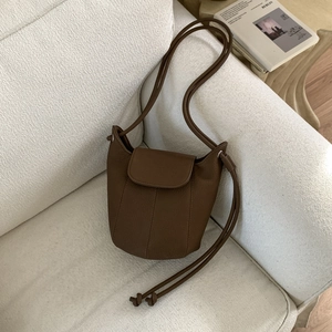 Close-up of brown bucket bag with stitched leather panels on a beige fabric sofa
