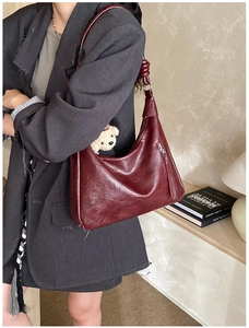 Dettaglio di una borsa hobo rosso scuro con tracolla annodata e ciondolo a forma di orsetto