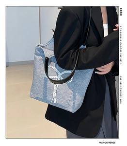 Detailed view of light blue denim tote bag with white lace bow on black blazer