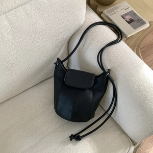 Detail of minimalist black bucket bag with knotted straps on a textured sofa