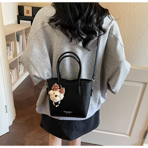 Détail d'un sac seau en cuir noir avec breloque d'ours porté par un mannequin de dos