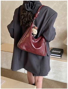 Dettaglio borsa hobo in pelle bordeaux testurizzata con tracolla annodata e ciondolo pompon