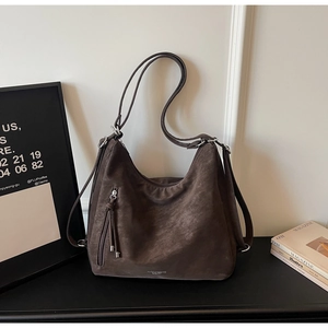 Detail view of large dark brown suede tote bag with side fringe and logo on black surface