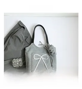 Detail of grey knitted tote bag featuring a white lace bow and black leather handle