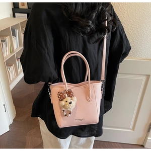 Sac seau rose avec breloque d'ours et bandoulière réglable, porté par un mannequin en intérieur