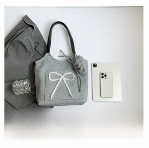 Detail view of grey fabric tote bag with lace bow decoration and black leather strap