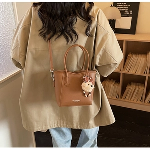Détail d'un sac seau marron avec charm ours en peluche dans un décor intérieur chaleureux