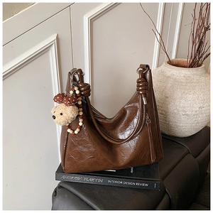 Dettaglio borsa tote in pelle marrone scuro con ciondolo orsetto di peluche e tracolla annodata
