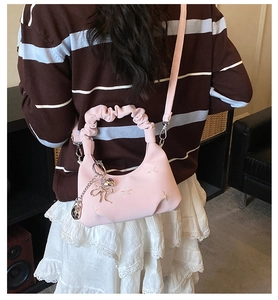 Detail showing pink dumpling bag with star embroidery and ruffled handle on shoulder