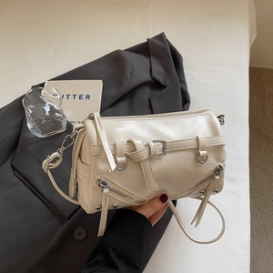 Detail der cremefarbenen Zylindertasche mit Nieten und Reißverschlüssen auf Anzug