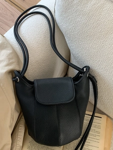 Minimalist black lychee pattern leather bucket bag with slim straps on soft background