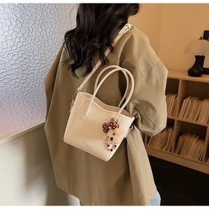 Vue détaillée du sac seau blanc crème avec breloque d'ours porté par un mannequin