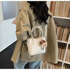 Gros plan d'un sac seau en cuir crème avec breloque ours sur un fond de bibliothèque