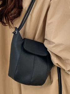Minimalist black lychee leather bucket bag for women styled with casual trench coat