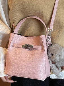 Pink lychee texture bucket bag with silver lock and plush charm on knit background
