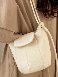 Minimalist cream textured leather bucket shoulder bag worn with an elegant trench coat