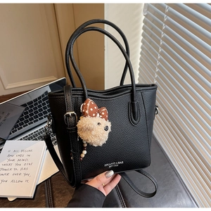Gros plan sur un sac seau en cuir noir grainé avec breloque ours à nœud papillon