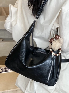 Elegante borsa a tracolla nera lucida con cinturino annodato e ciondolo a forma di orso