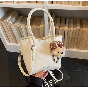 Détail du sac seau blanc crème à motif litchi avec breloque ours et bandoulière
