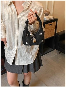 Detail of black pleated handbag with white floral embroidery and gold metal charms