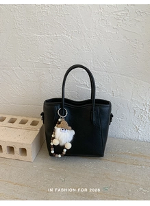 Détail du sac à main noir minimaliste avec charm monstre en peluche blanc texturé