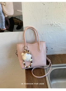 Sac seau rose en cuir mat avec charme en peluche et chaîne perlée sur planche en bois
