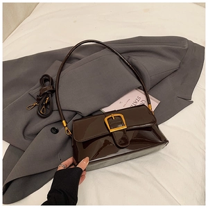 Detail der dunkelbraunen Lackleder-Schultertasche mit Goldschnalle auf schickem Anzug
