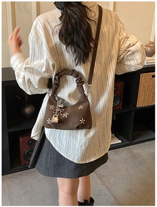 Close-up of brown pleated handbag featuring silver star studs and metallic lock charm