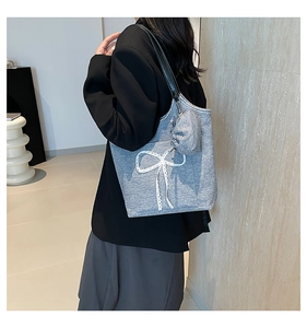 Close-up of a grey knit tote bag with a white lace bow and black leather handles