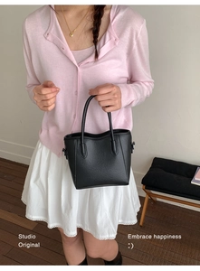 Sac à main noir minimaliste porté avec un pull en maille rose et une jupe en dentelle