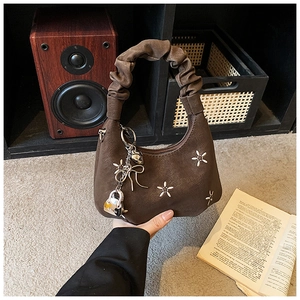 Detail of dark brown croissant bag featuring floral embroidery and metal pendants