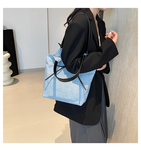 Detail of light blue denim tote bag with black leather handles and drawstring ribbons