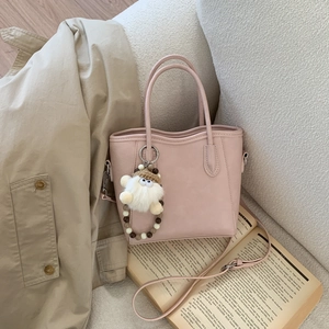 Détail du sac seau en cuir rose avec charm en fourrure blanche sur fond de tissu neutre