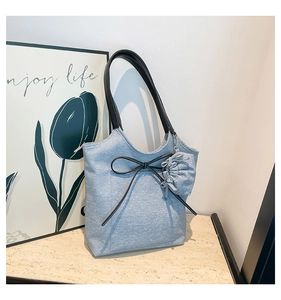 Detail of light blue denim tote bag with black bow and small ruffled side pouch
